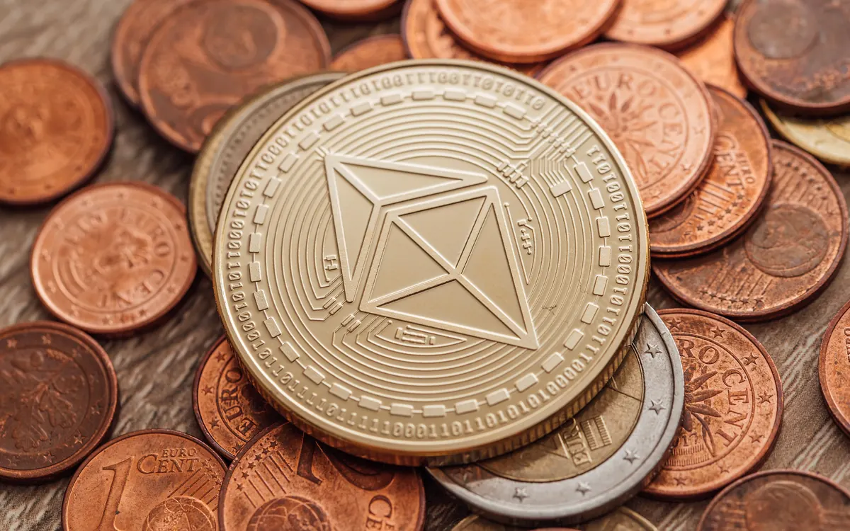 Золотистая физическая монета Ethereum на горке медных и серебряных монет (иллюстративное фото)