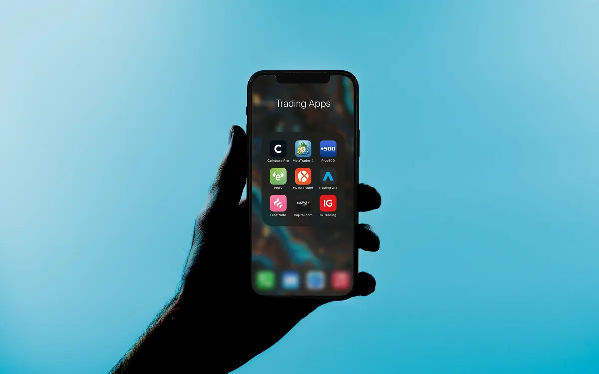 A smartphone showing a folder of trading apps, held against a blue background (illustrative photo)