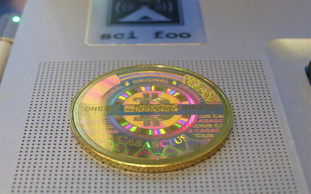 A gold-coloured Casascius physical bitcoin coin lying on a grey surface (illustrative photo)