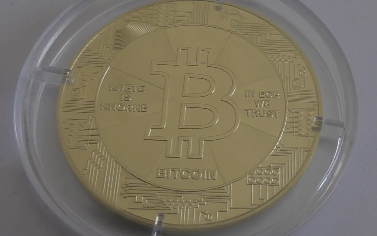 A gold-coloured physical bitcoin coin in a clear plastic capsule (illustrative photo)