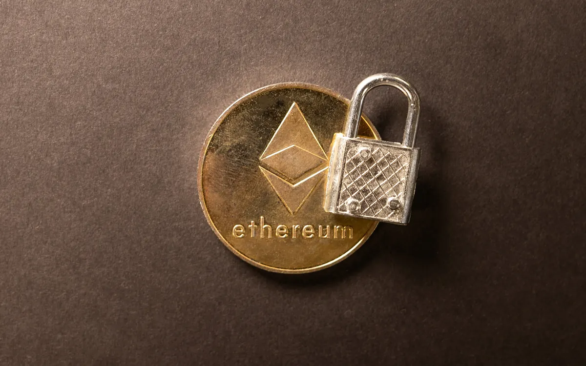 Золотиста монета Ethereum поруч із маленьким сріблястим замком на темному тлі (ілюстративне фото)