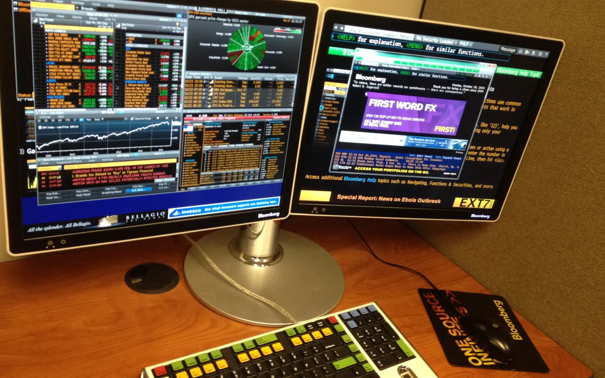 Two Bloomberg Terminal screens full of market data with the terminal's colour-coded keyboard on a desk (illustrative photo)