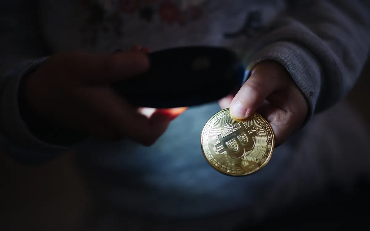 Детская рука держит золотистую физическую монету биткоина в луче фонарика (иллюстративное фото)