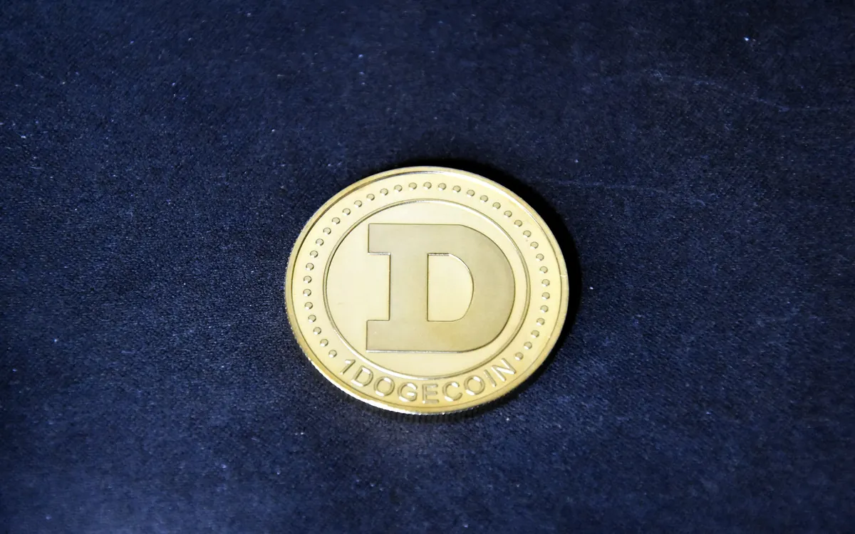 Gold-coloured physical Dogecoin coin with a large D on a dark blue fabric background (illustrative photo)