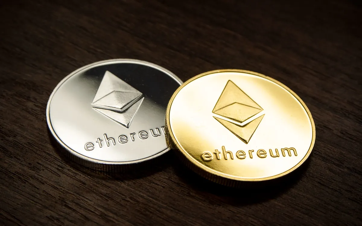 Silver and gold Ethereum commemorative coins on a dark wooden surface (illustrative photo)