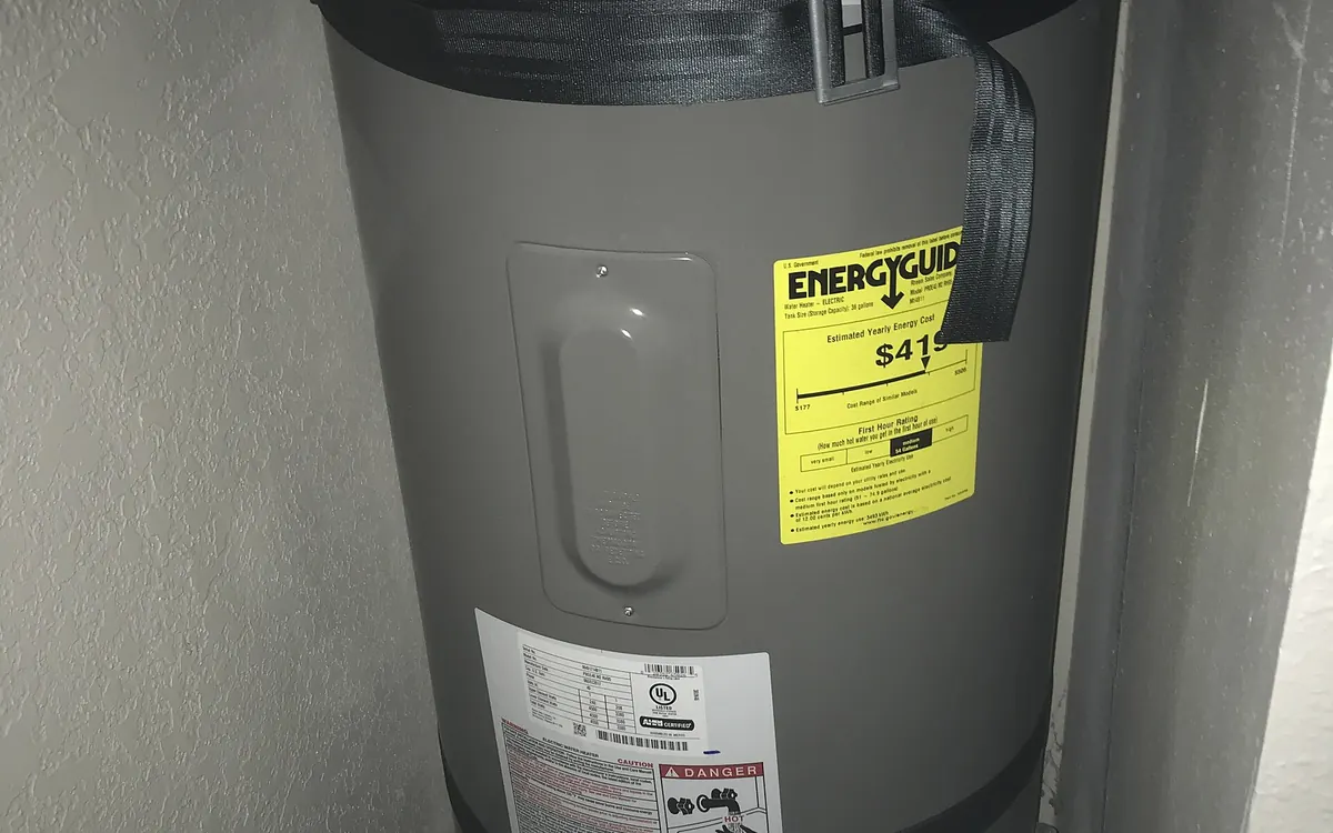 A grey 40-gallon Rheem electric water heater with a yellow EnergyGuide label in a utility closet (illustrative photo)