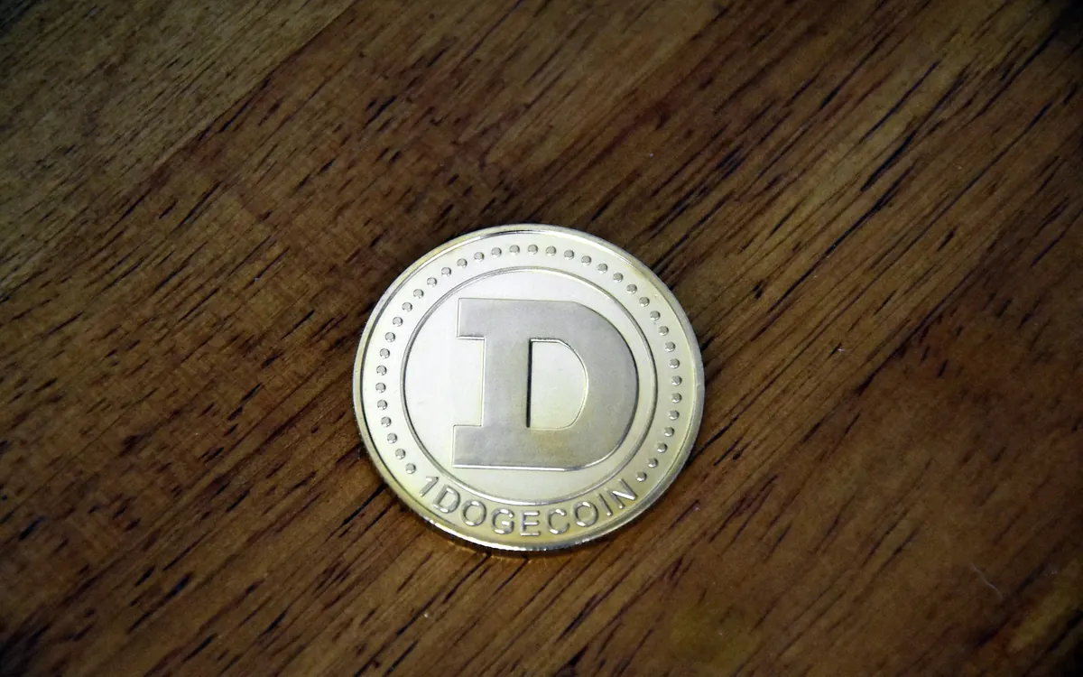 A silver-coloured physical Dogecoin coin lying on a dark wooden table (illustrative photo)