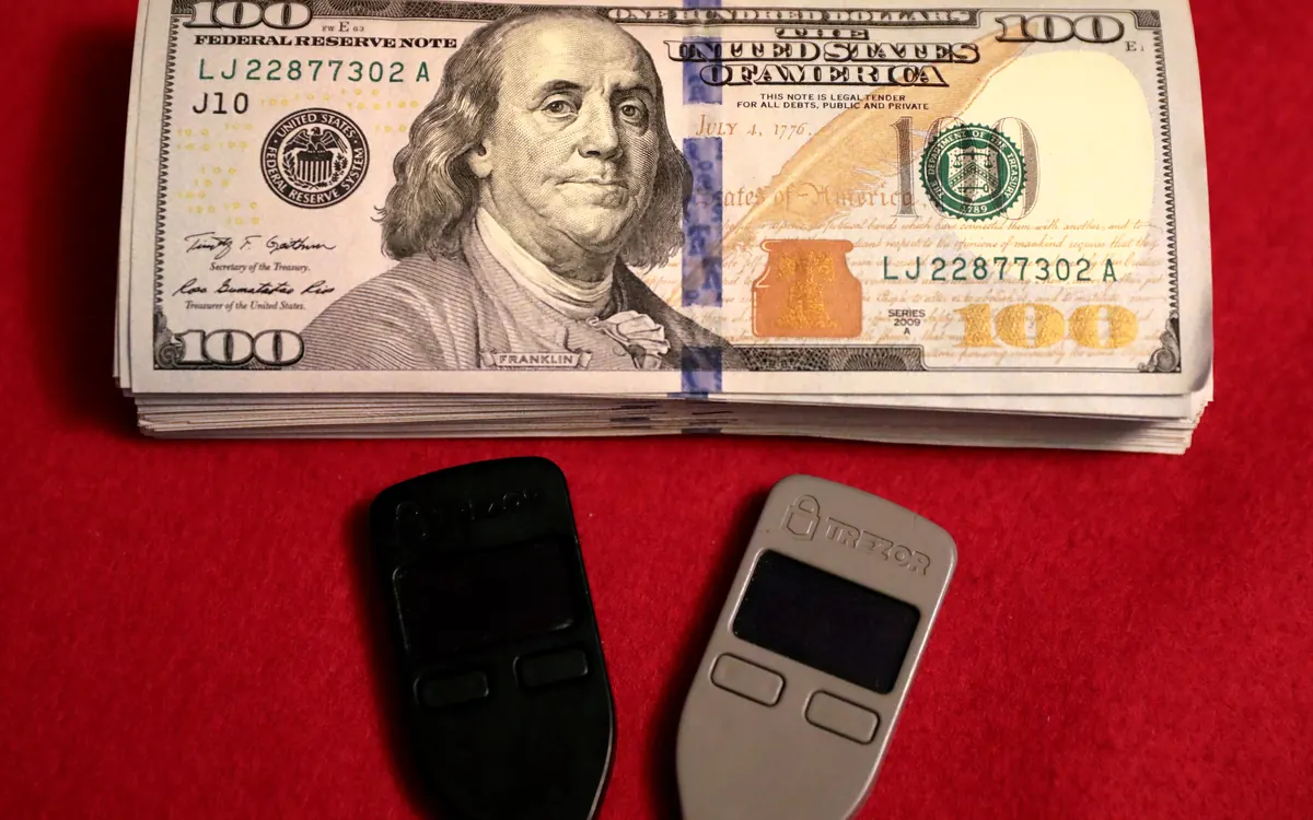 Two Trezor One hardware wallets lying on U.S. dollar banknotes