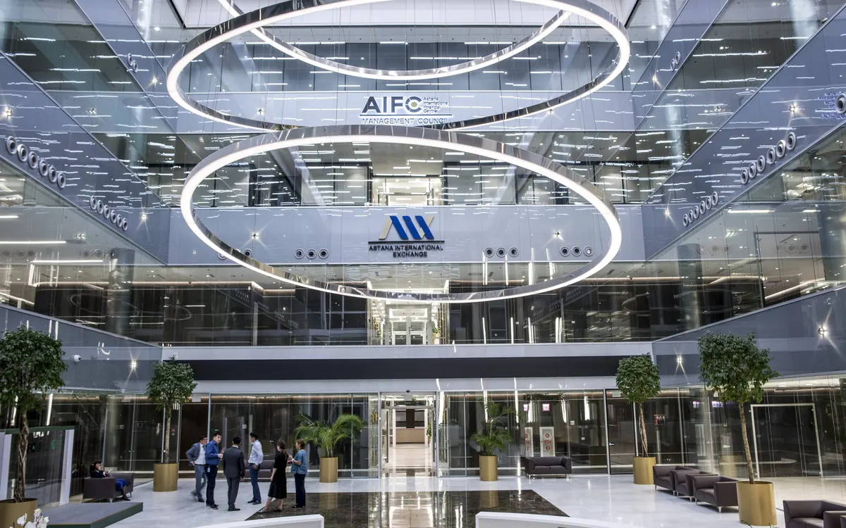 Атриум Международного финансового центра «Астана» с вывеской AIFC и логотипом Astana International Exchange под кольцевыми светильниками