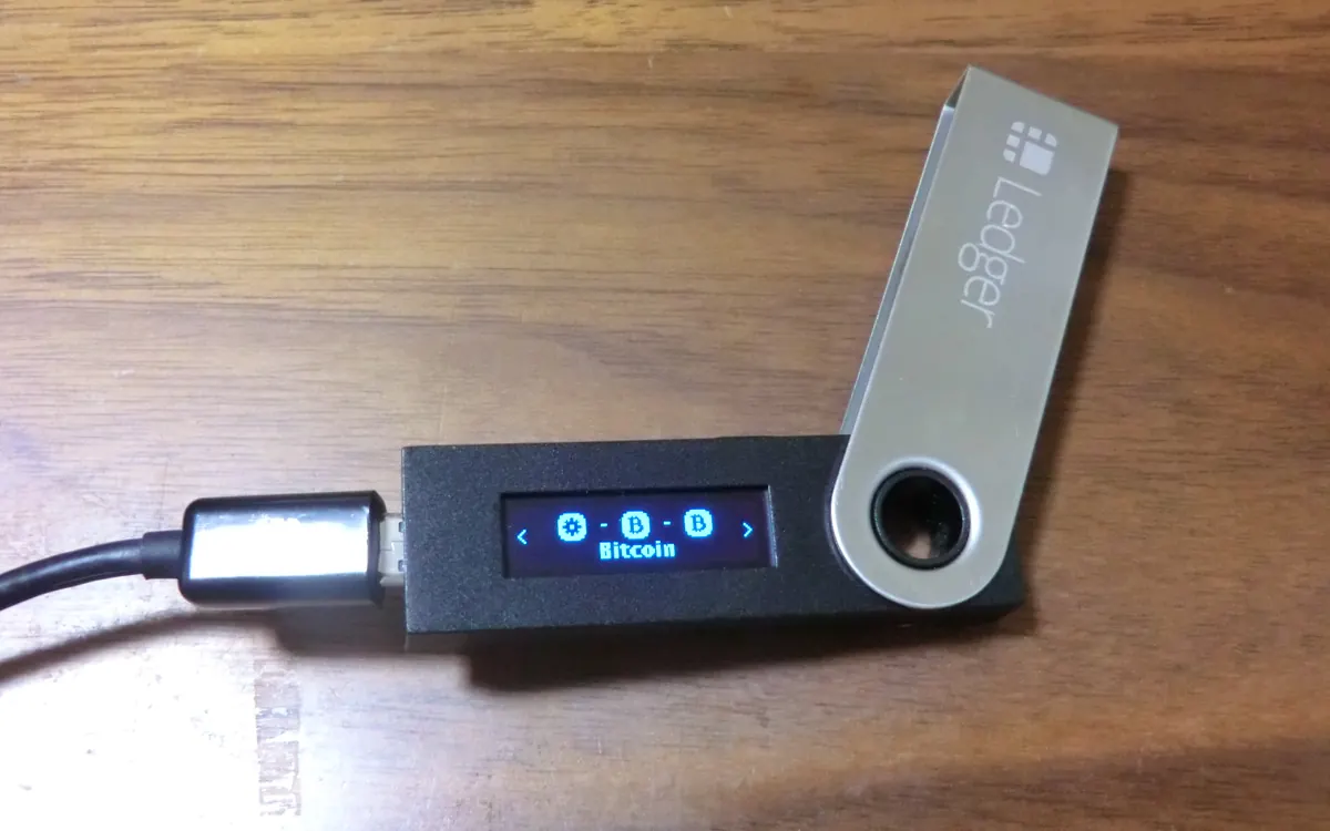 A hardware crypto wallet plugged into a USB cable on a wooden desk (illustrative photo, not a Keystone device)