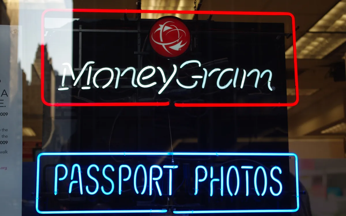 Красная неоновая вывеска MoneyGram в витрине над синей вывеской Passport Photos (иллюстративное фото)