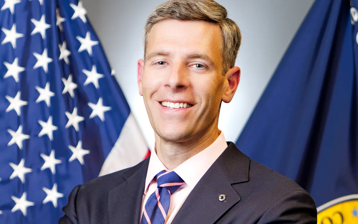 Official portrait of Comptroller of the Currency Jonathan Gould in front of US and OCC flags