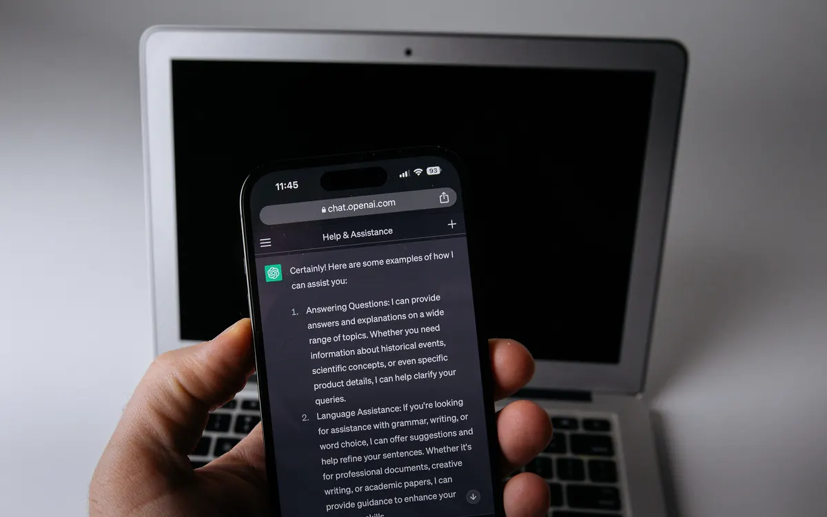 Smartphone showing the ChatGPT app in front of a laptop (illustrative photo)
