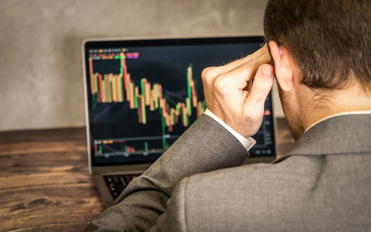 A trader holds his head in front of a laptop showing a falling candlestick chart (illustrative photo)