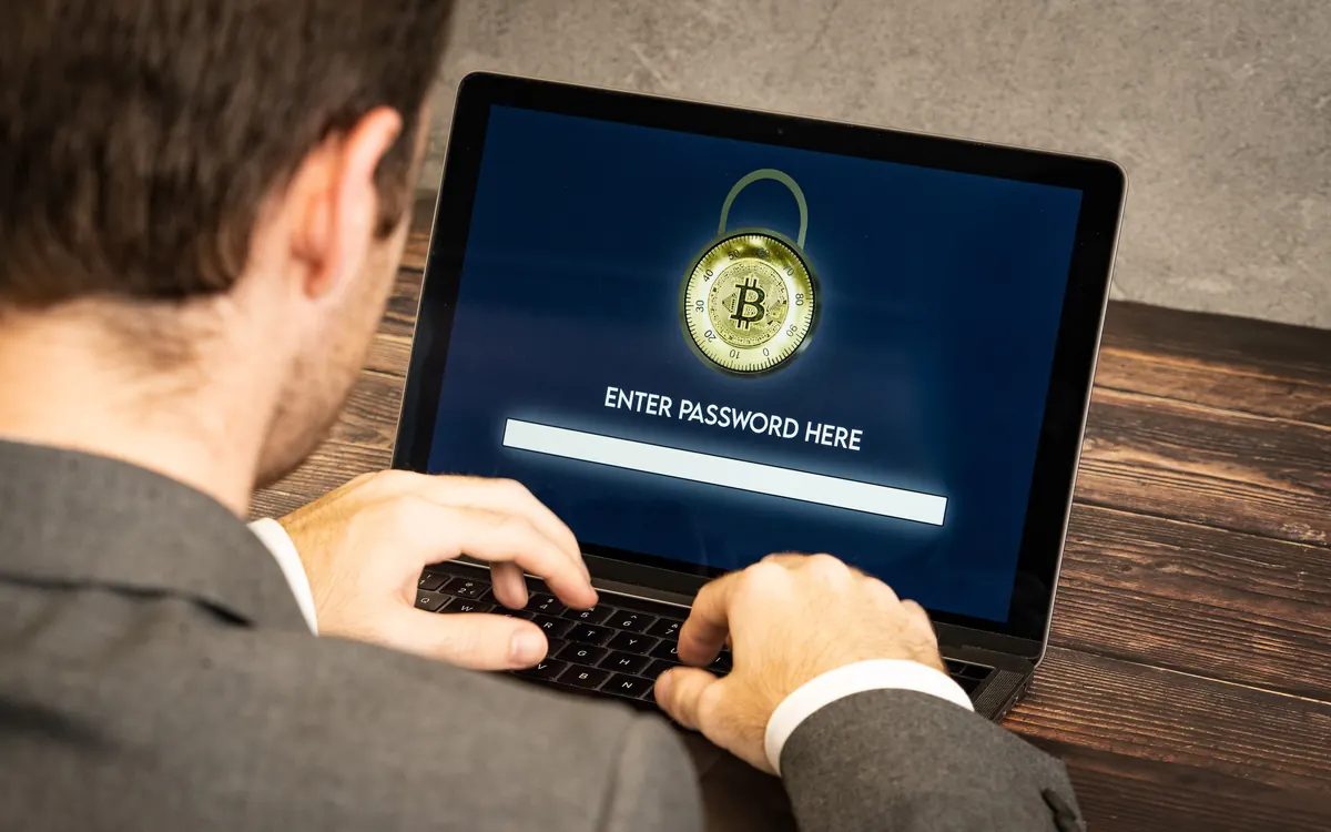 A person typing a password on a laptop next to crypto coins (illustrative photo)