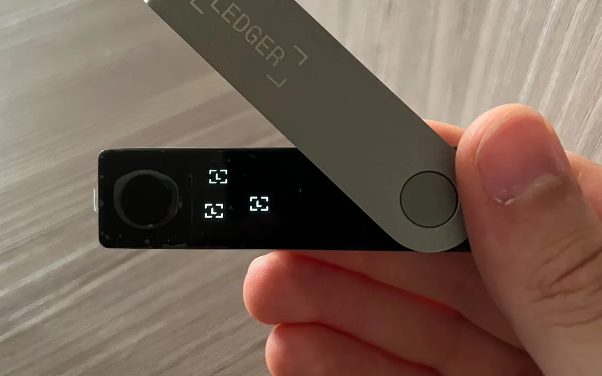 A Ledger Nano X hardware wallet held in a hand (illustrative photo)