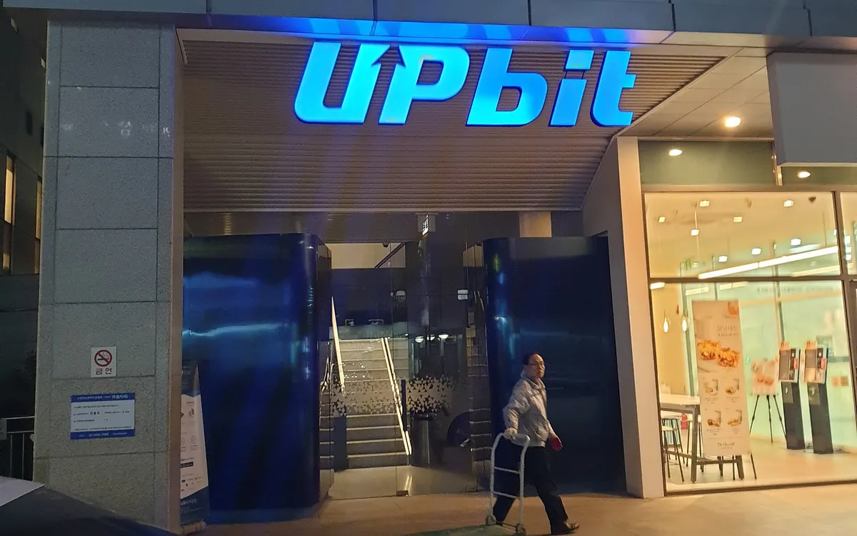 Entrance of an Upbit crypto exchange office in South Korea with the blue Upbit sign lit up at night