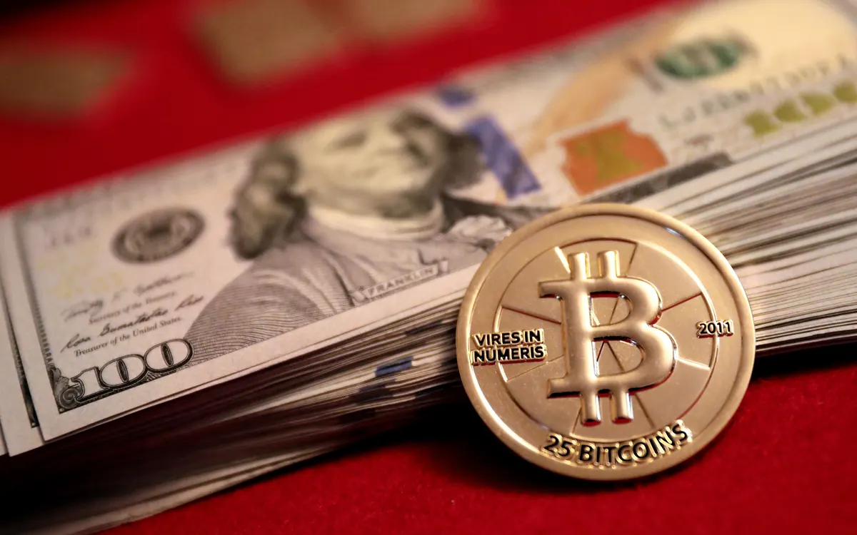 Золотая физическая монета Casascius на 25 BTC лежит на пачке стодолларовых купюр (иллюстративное фото)