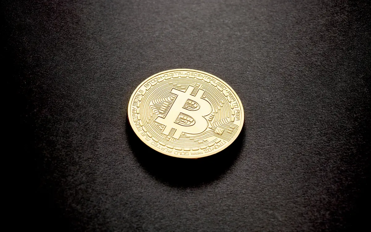 A single physical bitcoin coin lying on a dark surface (illustrative photo)