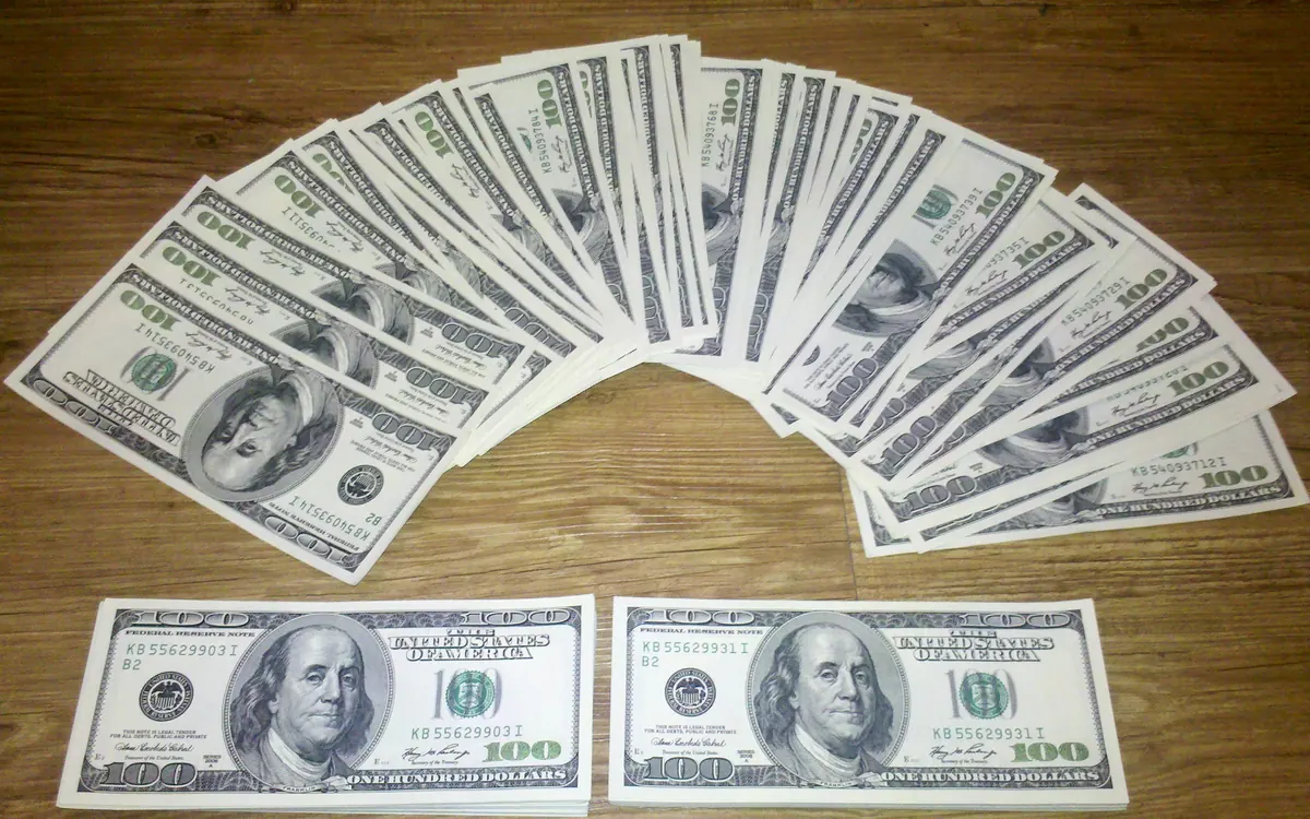 A fan of US hundred-dollar bills on a wooden table, the currency RLUSD tracks (illustrative photo)