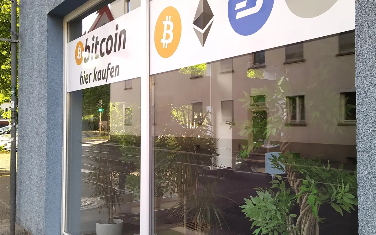 A crypto exchange shop window with Bitcoin, Ethereum, Dash and Litecoin logos and a 'Bitcoin hier kaufen' sign (illustrative photo)