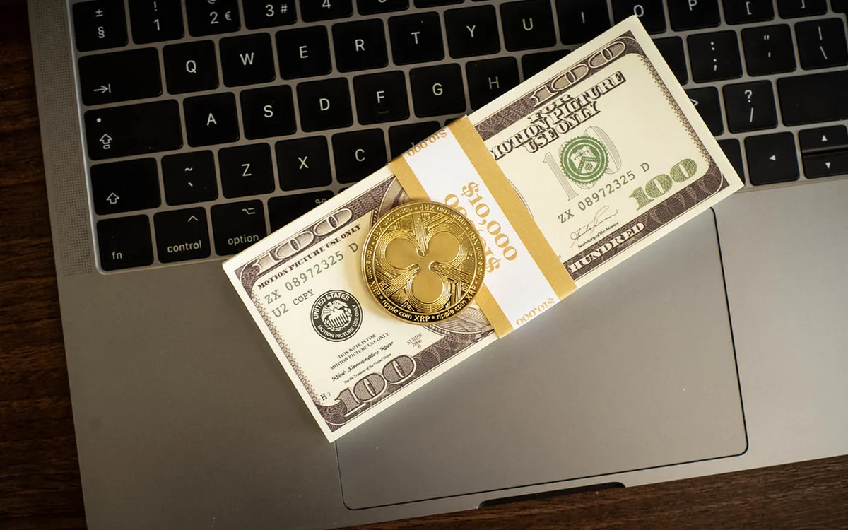 Gold-coloured XRP coin resting on a bundle of $100 bills on a laptop (illustrative photo)