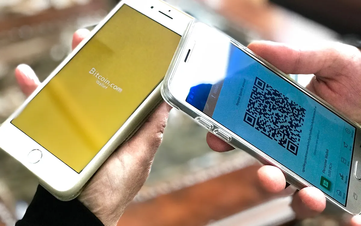 Двое людей держат смартфоны с открытыми криптокошельками, на одном — QR-код для платежа (иллюстративное фото)